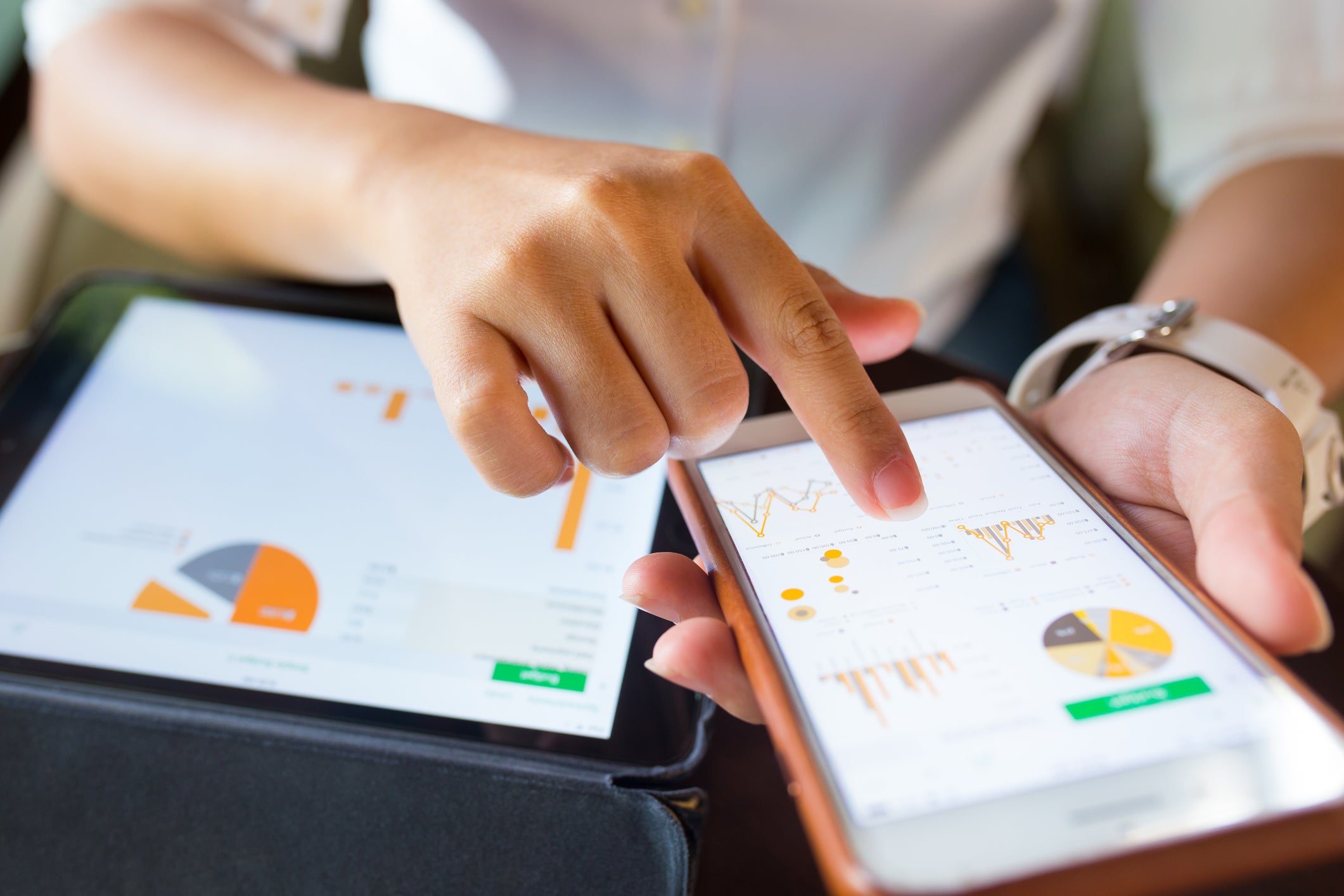 Closeup of a phone and tablet displaying charts and graphs. A woman is tapping the phone screen with her finger.